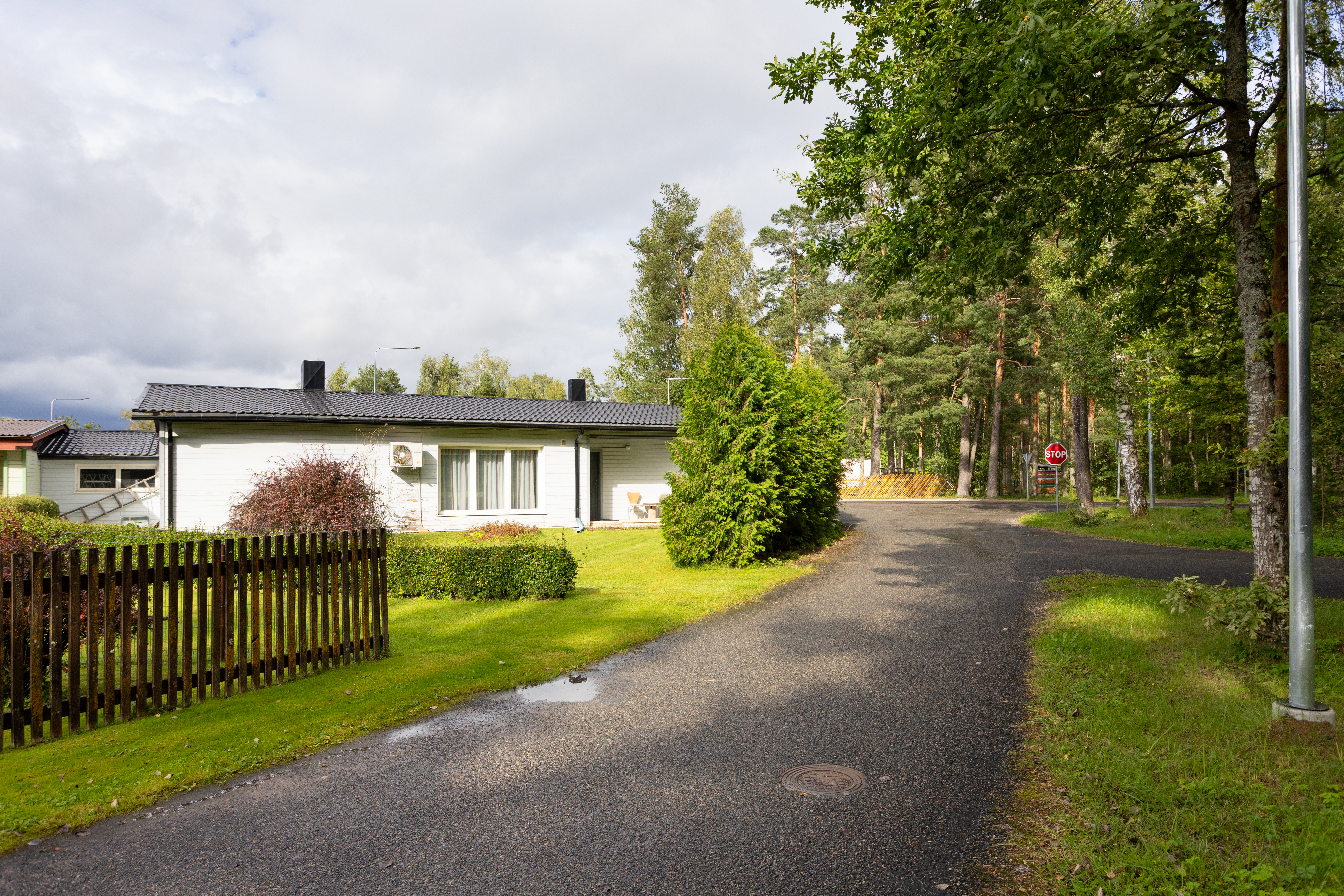 Ühekordne maja roheluses, puitlipp-aiaga ümbritsetud.